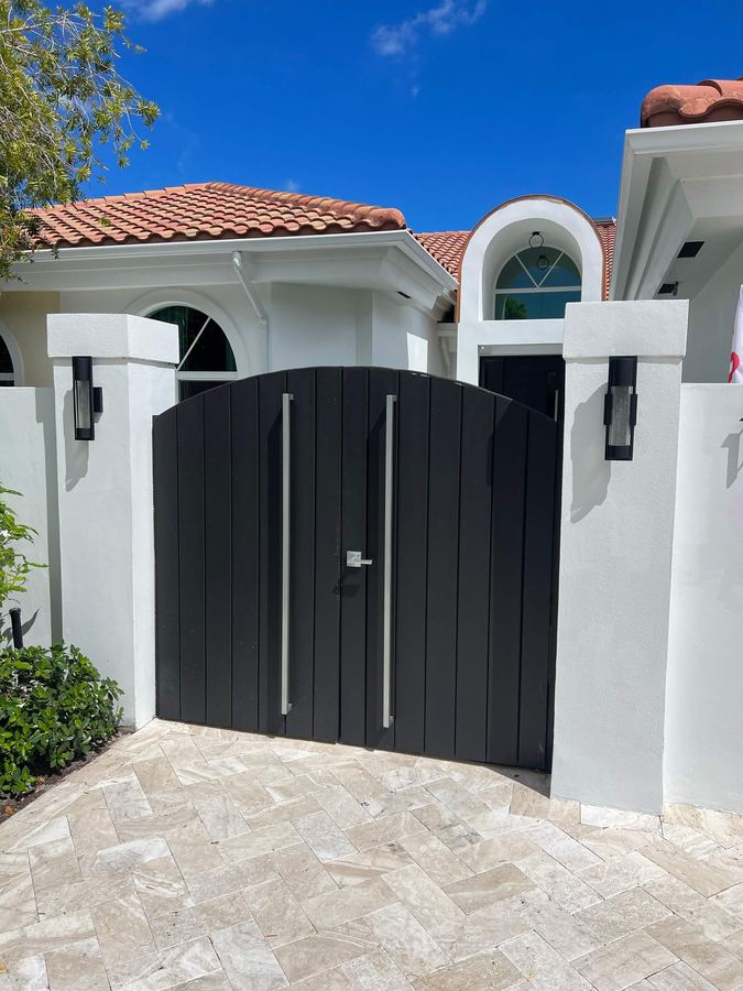 Black arched aluminum entry gate between stucco columns